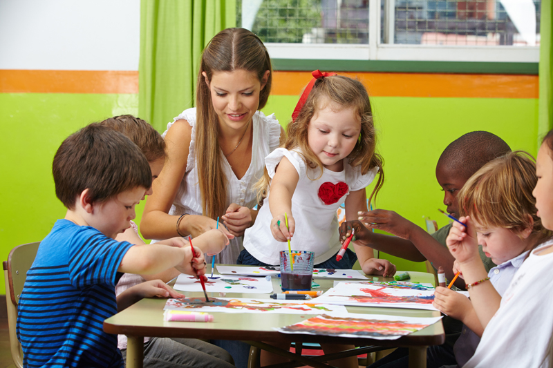 Viele Kinder malen mit Farbe zusammen mit Erzieher im Kindergarten